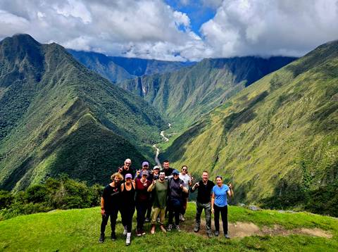       Trekkers celebrating on grassy lookout with sweeping valley and river below
  