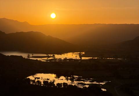       Golden sun setting behind dark hills with reflective wetlands glowing below
  