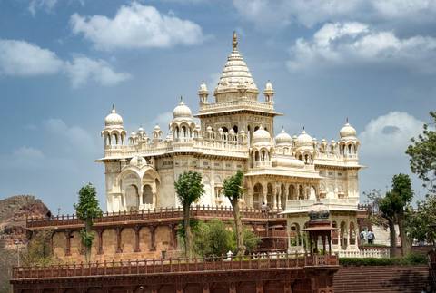       Elegant white marble cenotaph with domes and intricate carvings standing against a blue sky
  
