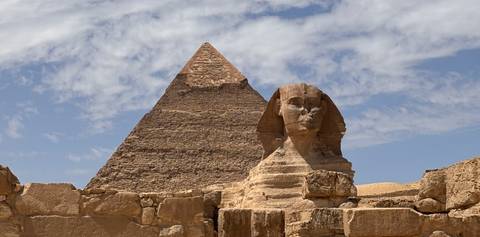       Iconic Sphinx statue set before the Great Pyramid under a bright blue sky with wispy clouds
  