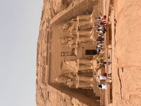       Massive rock-cut façade of Abu Simbel temple with colossal statues and crowds of visitors below
  