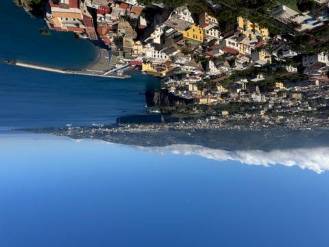       Panoramic overlook of Sorrento coastline with town rooftops, cliffs and sweeping blue bay under clear skies.
  