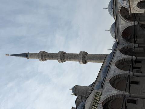       Tall slender minaret rising above courtyard arches against pale sky
  