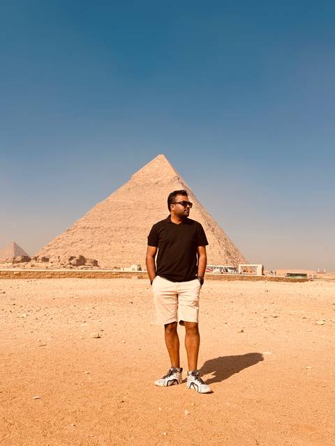       Man standing confidently before towering pyramid under clear sky
  