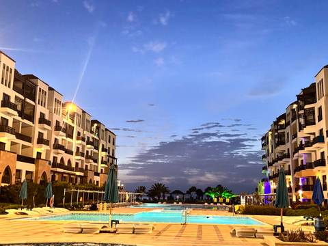       Resort pool flanked by modern white buildings against colourful dusk sky
  