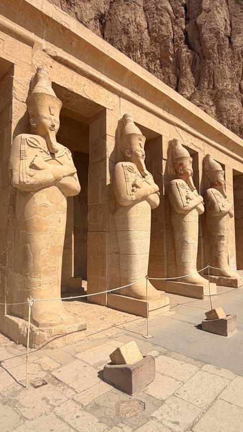       Row of colossal Osiride statues lining temple colonnade in bright desert sun
  