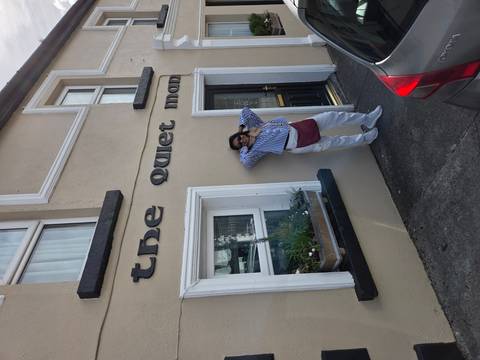       Traveler posing in front of a beige building bearing the sign 'the quiet man'.
  