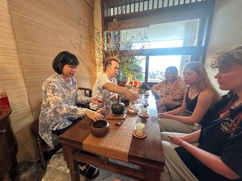       Small group at a wooden table participating in a traditional tea ceremony inside a cozy room.
  