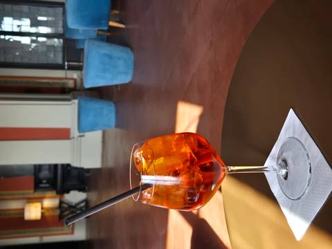       Close-up of an orange Aperol Spritz cocktail on a small table in a stylish lounge.
  