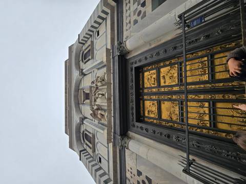      Upward view of the gilded Gates of Paradise on Florence Baptistery with visitors below
  
