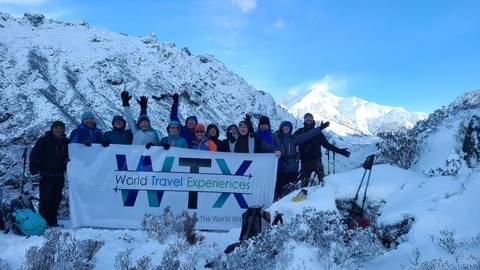       Cheerful trekking group holding 'WTX' banner amid snow-covered Himalayan landscape
  