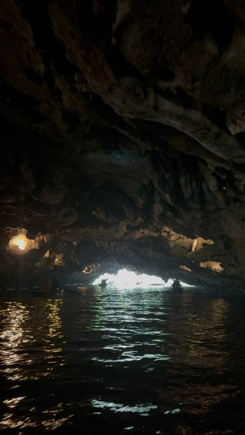       Dimly lit interior of a limestone cave with rough formations and a faint light source at the exit.
  