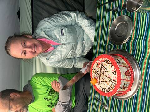       Smiling trekker inside a mess tent about to cut a decorated celebration cake on the Inca Trail.
  