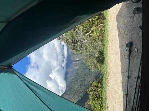       Mountain vista framed by an open tent doorway, revealing cloud-capped Andean peaks and a trekking pole resting on the ground.
  