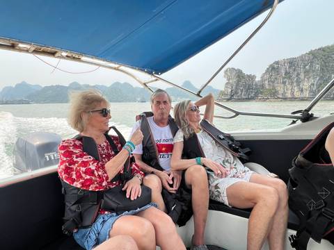       Three travelers cruise on a speedboat through emerald waters framed by limestone karsts in Halong Bay.
  