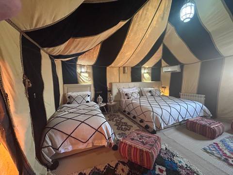       Comfortable desert glamping tent interior with patterned rugs and twin beds beneath canvas roof.
  