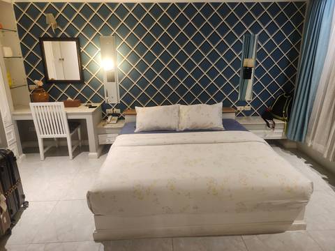       Neat hotel room with double bed, patterned blue feature wall, small desk and suitcase in the corner
  