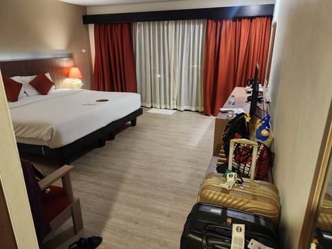       Spacious hotel room with king bed, red curtains and luggage near a long dresser
  