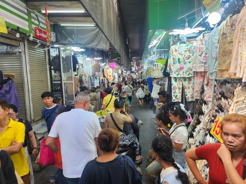       Crowded narrow indoor market aisle packed with shoppers and hanging clothes
  