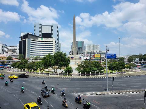       Victory Monument roundabout in Bangkok surrounded by traffic and modern buildings
  