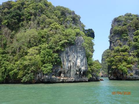       Towering limestone cliffs covered in lush greenery above turquoise bay water
  