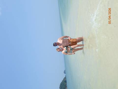       Couple standing in shallow clear sea under bright blue sky with date stamp visible
  
