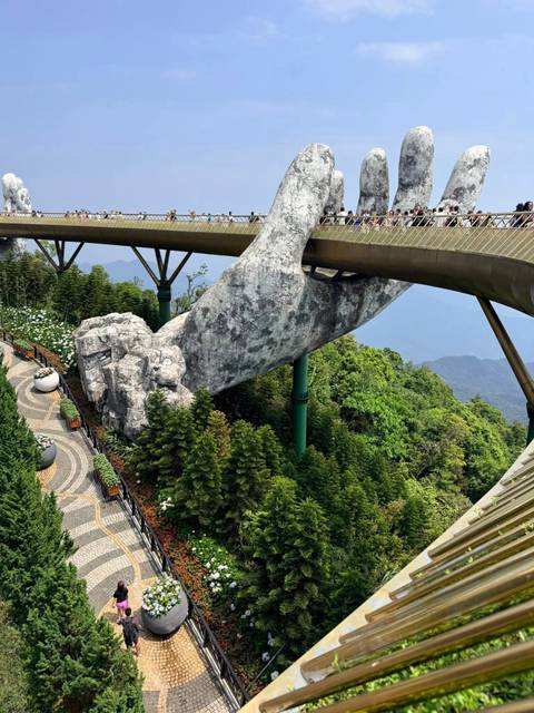       Golden Bridge held by giant stone hand above lush forested hills
  
