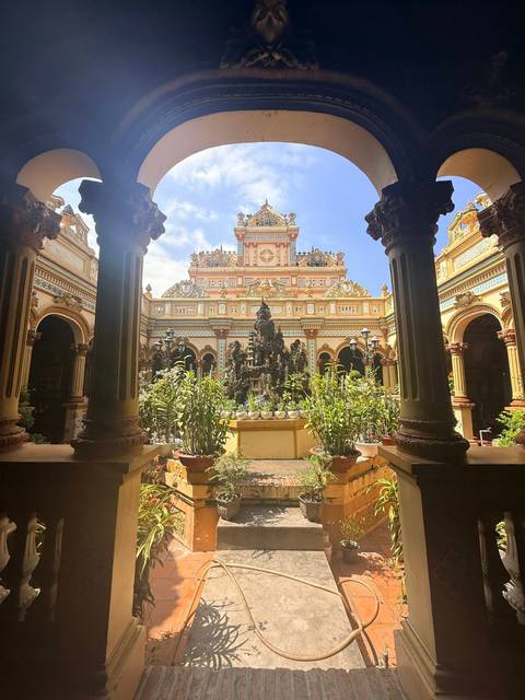       Elegant courtyard of Vinh Trang Temple framed by ornate columns and potted plants
  