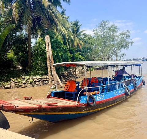       Blue wooden boat with life jackets navigating muddy Mekong Delta waters
  
