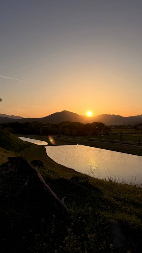       Golden sunset descending behind a silhouetted mountain ridge reflecting in rice paddies and ponds.
  