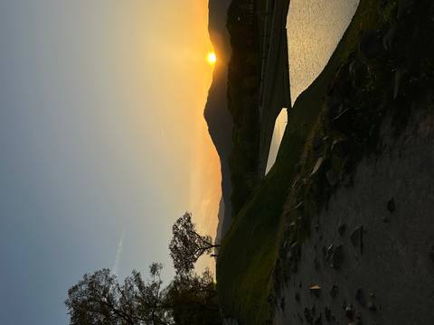       Serene sunset over grassy mound and reflective canal with distant hills silhouetted.
  