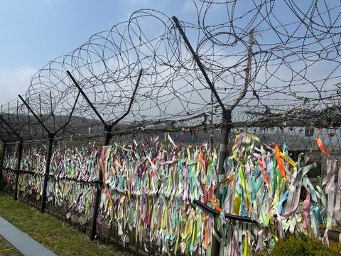       Fence topped with barbed wire and covered in multicolored prayer ribbons at DMZ.
  