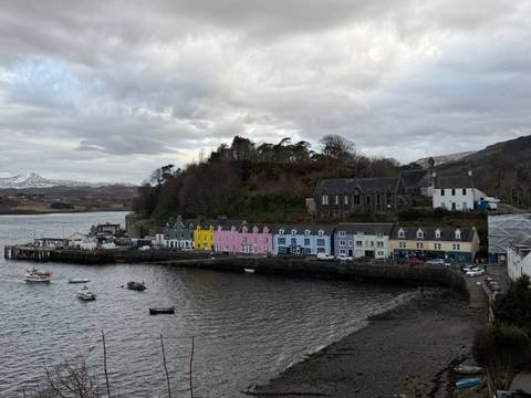       Harbor view of Portree with pastel waterside houses and moored boats under cloudy sky.
  