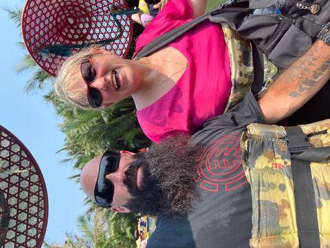       Smiling couple seated in a circular bamboo basket boat wearing life vests amid lush palms
  
