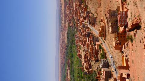       Expansive view of an arid valley town with green oasis patches under clear blue sky
  
