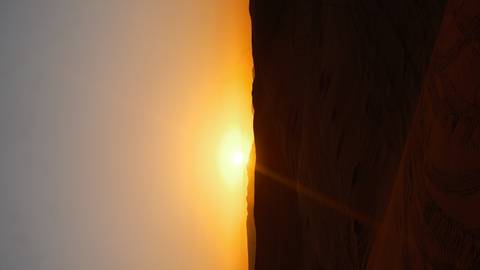       Orange sun setting over rolling desert dunes casting long shadows
  