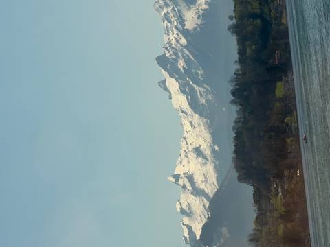      Snow-capped Swiss Alps rising above a tranquil lake with a hazy spring sky.
  