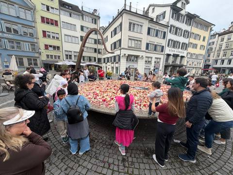       Crowd gathered around a large circular platform filled with colorful rose petals in Zurich’s historic district.
  