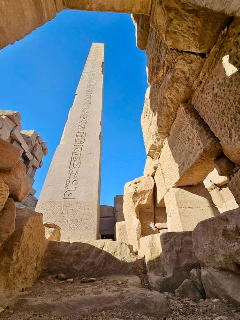       Sandstone obelisk with hieroglyphs framed by massive temple blocks against clear sky.
  