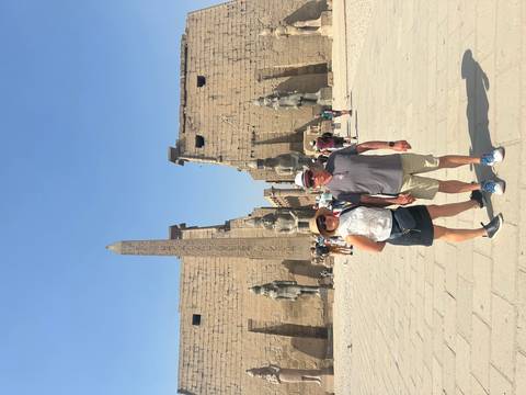       Travelers standing before giant statues and obelisk at Luxor Temple entrance.
  