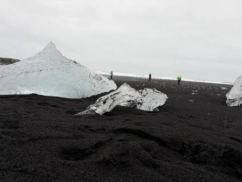      Large blue ice chunks rest on black volcanic sand as visitors explore Iceland’s Diamond Beach.
  
