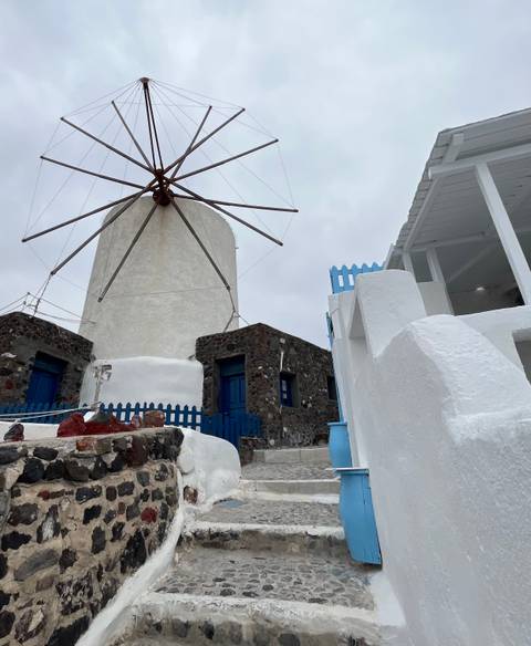       Traditional white windmill and stone house with blue doors on an overcast Greek island day.
  