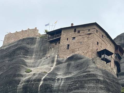       Stone monastery clings to dramatic grey cliffs of Meteora under hazy skies.
  