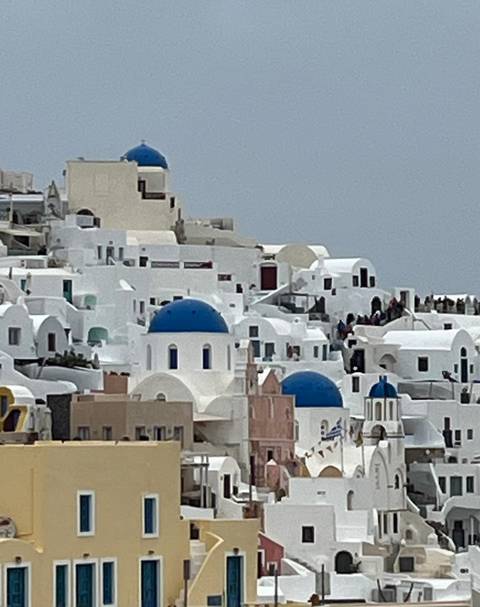       Cluster of white Cycladic houses with blue domes perched on Santorini’s caldera rim.
  