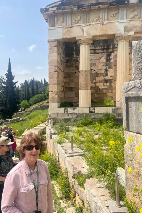       Visitors explore ancient stone columns and ruins surrounded by wildflowers at Delphi.
  
