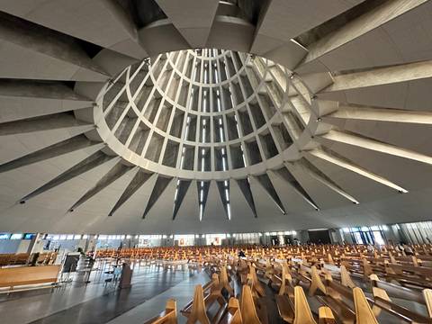       Sweeping interior of a modern circular basilica with soaring concrete ribs and wooden pews.
  