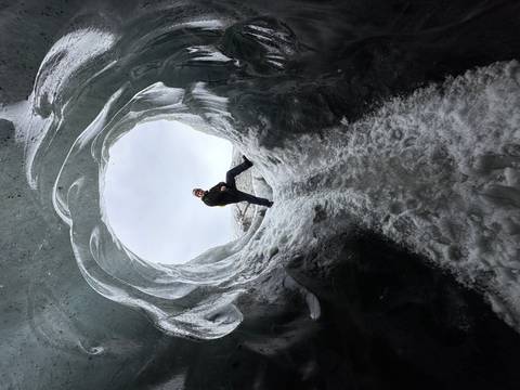       Adventurer poses inside a circular ice cave entrance framed by sculpted blue ice walls
  