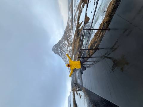       Excited traveller in a yellow jacket jumps for joy on a viewing platform with snow-capped Kirkjufell mountain behind
  