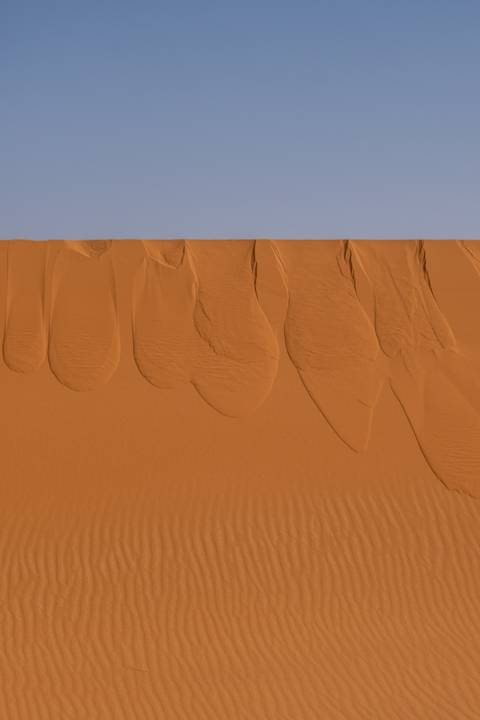       Aerial view of smooth orange sand dunes with elegant wind-carved ridges in the desert.
  