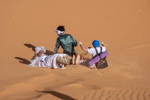       Three people slide playfully down a steep sand dune leaving trails in the fine desert sand.
  